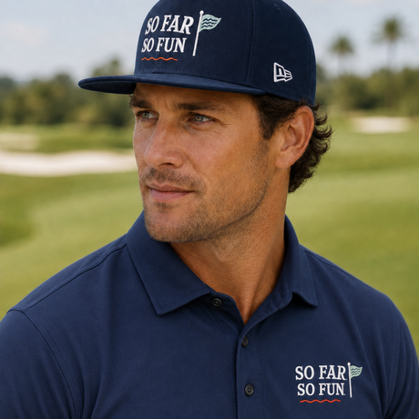 A man wearing a navy blue polo shirt and matching navy blue baseball cap with 'SO FAR SO FUN' text and a small New Era logo, photographed outdoors on a golf course.