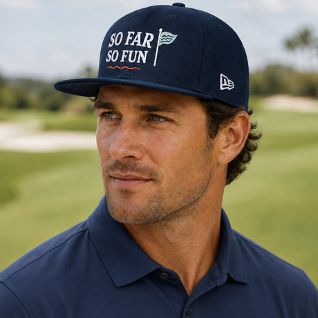 A man wearing a navy blue New Era baseball cap with 'SO FAR SO FUN' text and a matching navy polo shirt, photographed outdoors on a golf course.