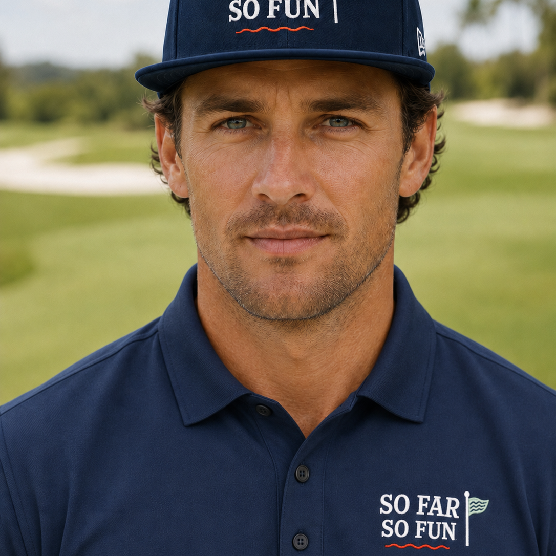 A man wearing a navy blue 'So Far So Fun' golf cap and matching polo shirt, standing on a golf course with a blurred background.