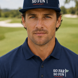 A man wearing a navy blue 'So Far So Fun' golf cap and matching polo shirt, standing on a golf course with a blurred background.