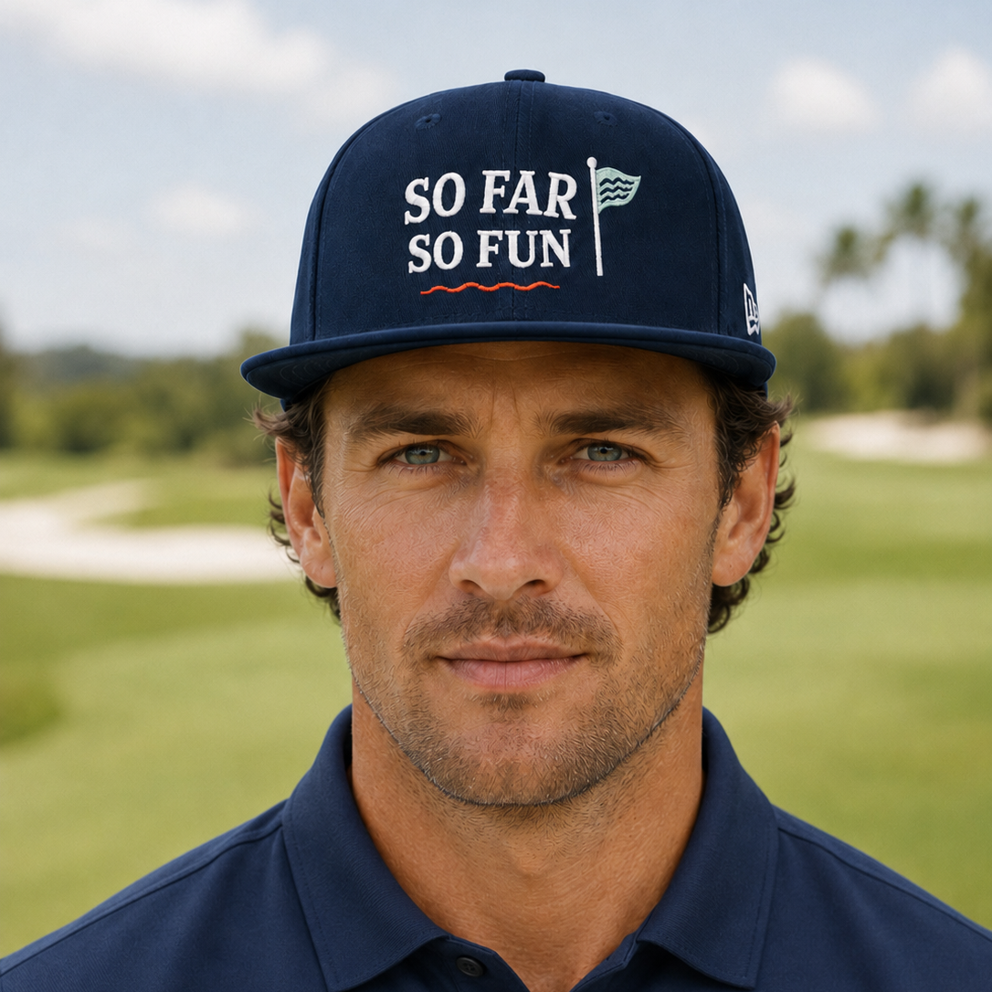 A man wearing a navy blue 'So Far So Fun' golf cap and matching polo shirt, standing on a golf course with a blurred background.